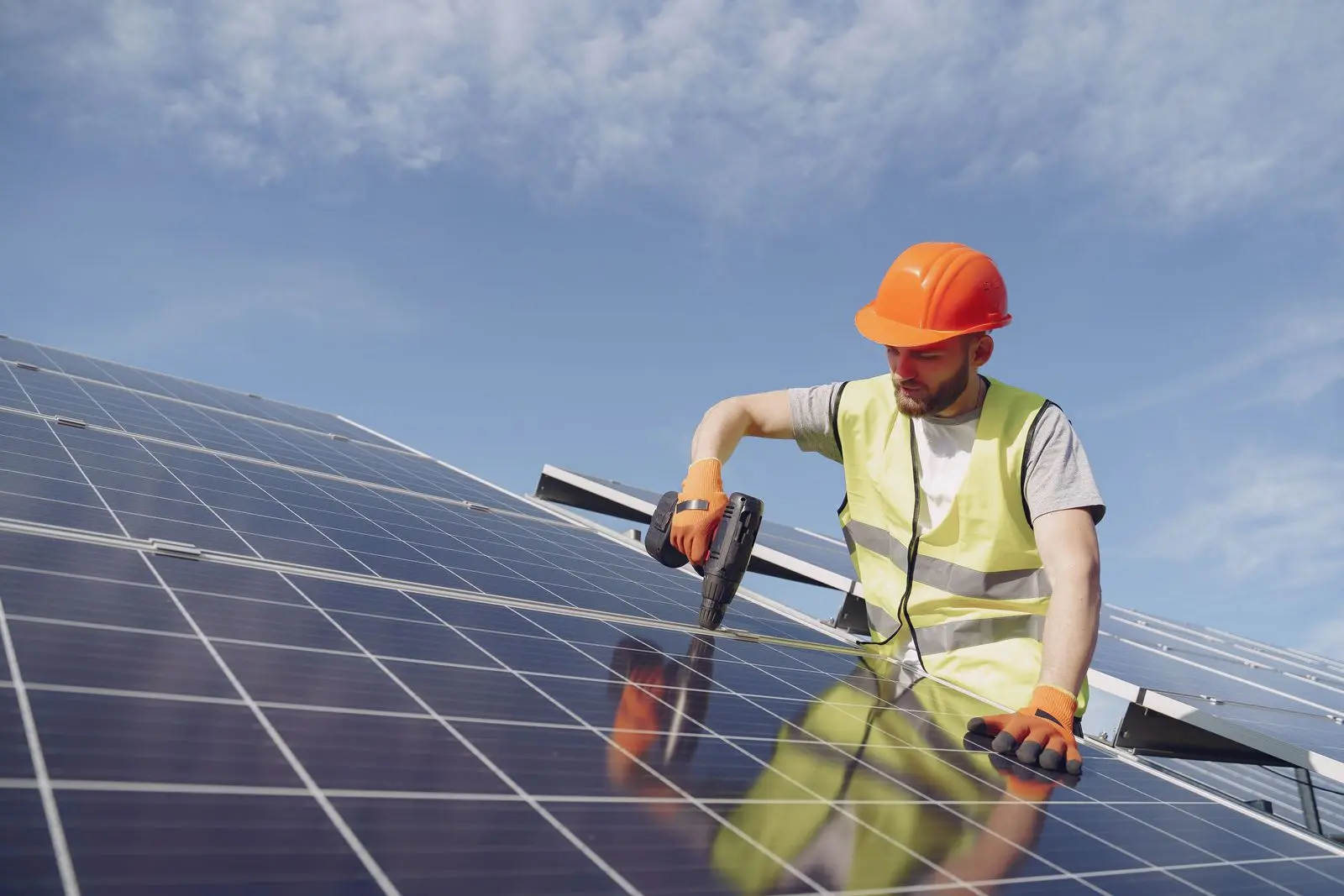A solar installer in hi vis fastening a panel on a roof.